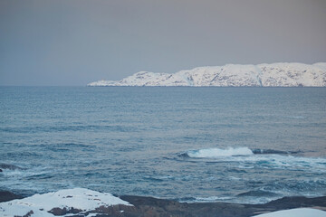 Obraz premium Winter arctic landscape. Non-freezing Barents Sea and snowy hills on the shore during the day