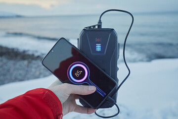 Charging a smartphone from a power bank against the backdrop of the sea and snow in winter