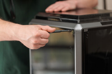Man using screwdriver while assembling 3D printer, concept of maintenance, repair and technology setup.