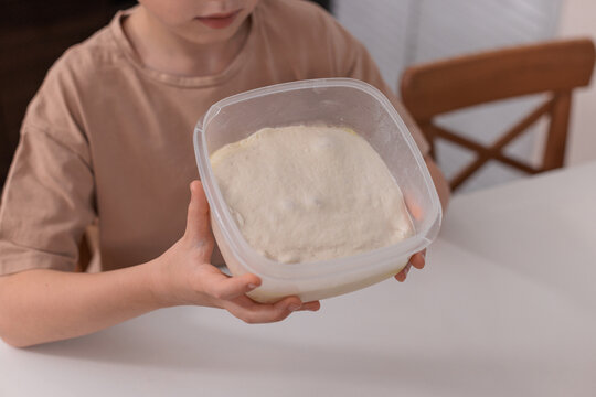 Child holding container with risen pizza dough, concept of baking and home food preparation. - Powered by Adobe