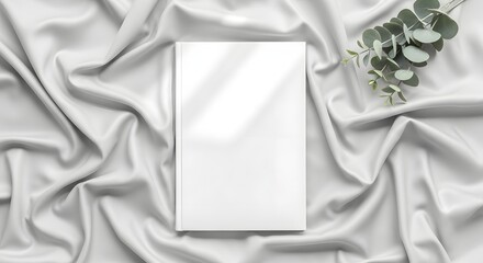 Blank white book cover on elegant draped fabric with eucalyptus