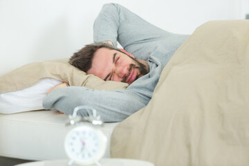 sleepy man holding alarm clock in bed