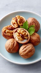 Close up rustic flat lay of whole and halved walnuts arranged on a light blue ceramic plate with green mint leaves accenting the warm brown nuts on a textured grey background