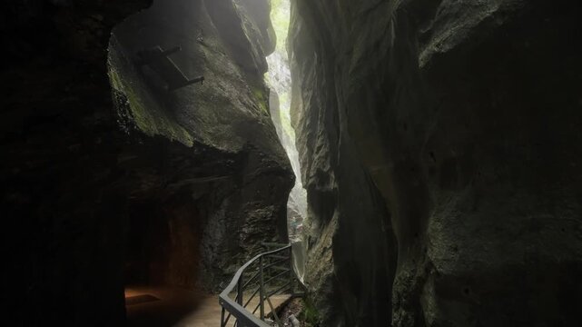 Traveler silhouette walking on a narrow path inside a dramatic gorge in the Swiss Alps. Majestic rock walls, mist, and adventure exploration in nature