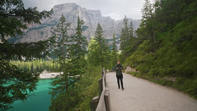 Static shot of a backpacker walking near the lake at Lago di Braies, Dolomites, Italy, surrounded by alpine mountains and forest