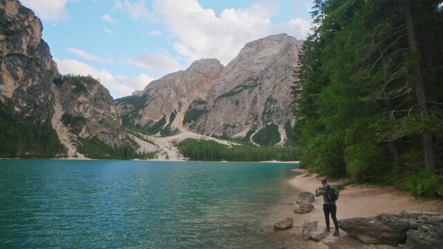 Hiker with backpack walking away from a rock near Lago di Braies in the Dolomites, Italy. Outdoor travel, freedom, and adventure lifestyle in the Alps