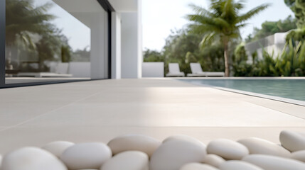 Zen-like outdoor scene with smooth white stones bordering a tiled patio, leading to a serene pool and lush greenery. A modern villa provides an elegant backdrop.