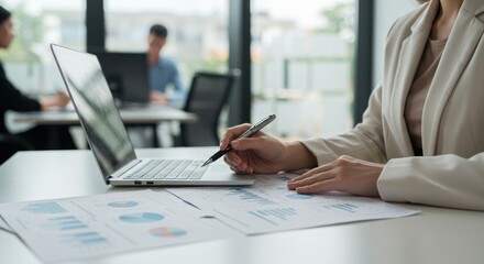 Woman works at a desk with laptop and documents in an office setting.