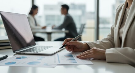 Woman working with laptop and documents in office setting with colleagues.