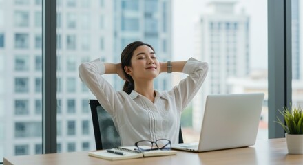 Woman relaxes at desk with laptop hands behind head in office setting.