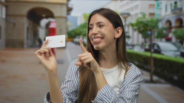 Smiling young hispanic woman holding white card with finger pointing to card on busy city street; excitement.