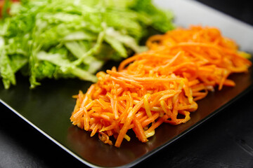Freshly shredded orange carrots and green lettuce arranged on a black plate, showcasing vibrant colors and textures, ideal for healthy meal preparation and culinary presentations