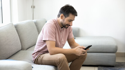 Obraz premium Middle-aged man using smartphone on sofa in modern living room