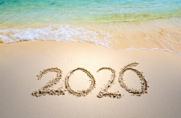 Happy New Year 2026, lettering on the beach with wave and clear blue sea. Numbers 2026 year on the sea shore, message handwritten in the golden sand on beautiful beach background. New Year concept.