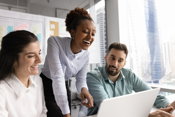 Overjoyed millennial business team laughing together reviewing project on notebook