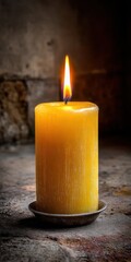 A warmly lit yellow candle burns brightly on a rustic surface.