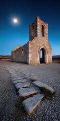 Atmospheric image of an old stone church ruin under a clear blue sky, illuminated by the setting sun.