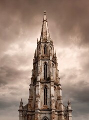 Dramatic, low-angle view of an aged Gothic church spire reaching into a stormy sky.