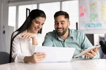 Joyful businesswoman doing paperwork with male teammate in Agile office