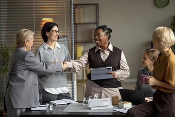 Middle Aged Caucasian Woman Shaking Hands with Middle Aged Black Woman in Office