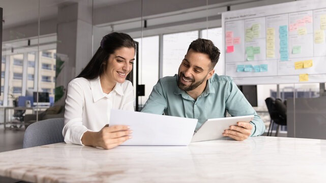 Two diverse businesspeople study paper digital documents at office table