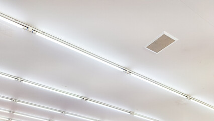 A series of LED tube lights installed on a ceiling. A row of lights are hanging from the ceiling in a room. The lights are white and are evenly spaced.