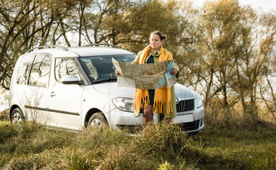 Young woman  traveler at a car with backpack and map searching destination on a road.