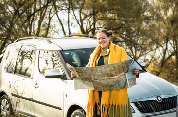 Young woman  traveler at a car with backpack and map searching destination on a road.