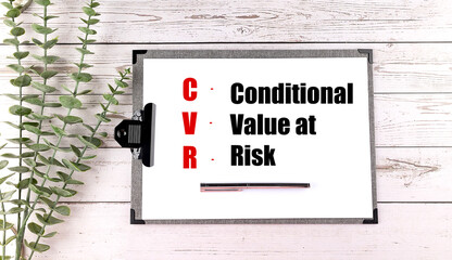 Clipboard with CVaR abbreviation for conditional value at risk on paper with pen and green leaves on wooden background