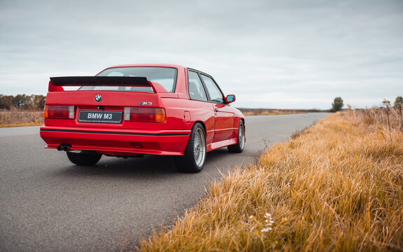 Red BMW coupe on a rural road on autumn day. Three quarter rear view of 1980s performance version of german coupe on empty road, lone tree on the horizon. Ukraine - October 19 2024