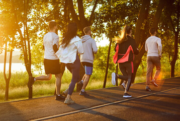 Rear view of a team of people running at sunset, engaging in group jogging, boosting sport training, uniting as runners, enhancing workout effort in a scenic outdoor fitness setting.