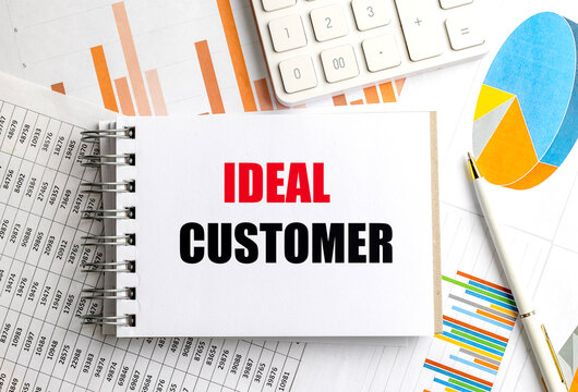 Notebook with ideal customer text on desk with charts, graphs, calculator and pen representing target audience analysis