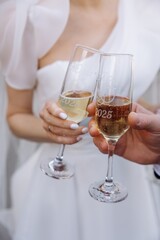 Bride and groom hands toasting with personalized champagne flutes engraved with '2025' and custom lettering on their wedding day