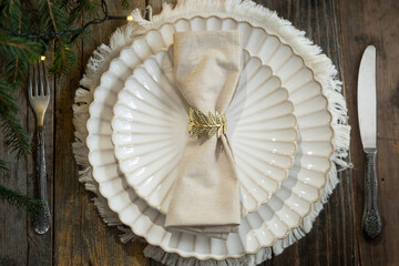 Elegant Christmas table setting with white plates, beige napkin, and decorative napkin ring. 