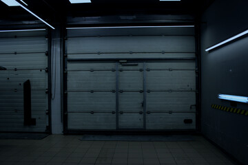 Obraz premium Empty workshop bay with two vertical roller shutter gates illuminated by industrial lamps 