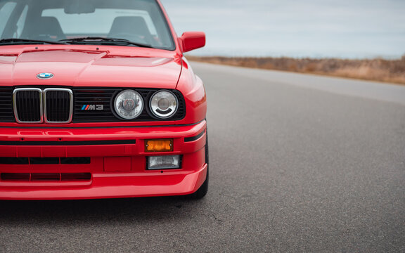 Left front side of BMW M3 E30 on a road (horizontal image). Front part of red 1980s high-performance BMW parked on a side of the road in a field. Ukraine - October 19 2024