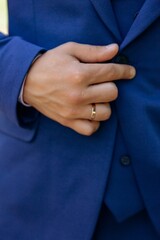Close-up of the groom's hand with a gold wedding ring buttoning or adjusting the lapel of his vibrant blue suit jacket