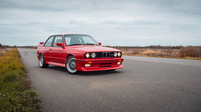 Red BMW coupe on a rural road on autumn day. Three quarter front view of M3 E30 - performance version of 1980s german sport coupe. Ukraine - October 19 2024