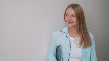 Obraz premium A portrait of a blonde businesswoman in a classic shirt standing in an office against a white wall, looking thoughtful. Coworking space for freelancers. Remote work. Banner for office workers.