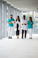 Fototapeta premium Diverse medical team walking hospital hallway discussing patient records