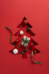 Naklejka na ściany i meble A red background featuring a stylized Christmas tree cutout filled with ornaments and a striped gift tied with a green ribbon, capturing festive mood, gifting, and holiday cheer Naklejka na ściany i meble A red background featuring a stylized Christmas tree cutout filled with ornaments and a striped gift tied with a green ribbon, capturing festive mood, gifting, and holiday cheer