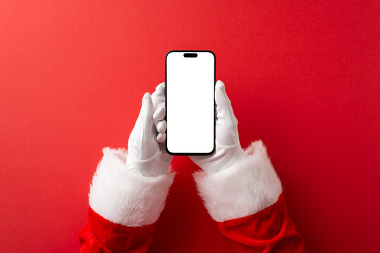 A festive scene shows gloved hands in a Santa suit holding a smartphone with a blank screen against a bold red backdrop, conveying modern holiday greetings and seasonal cheer