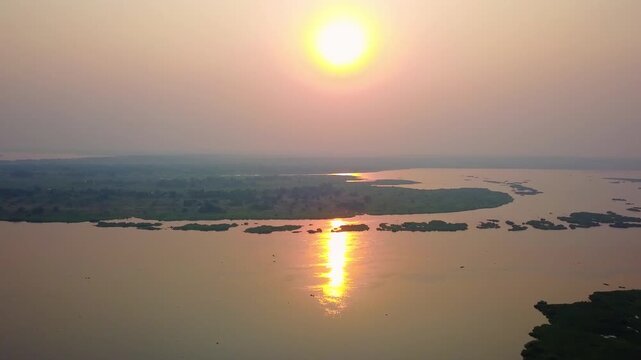 Sun sets over the calm water of Victoria Nile reflecting orange light on papyrus Cyperus papyrus and elephant grass Pennisetum purpureum in Murchison Falls National Park Uganda riverine habitat