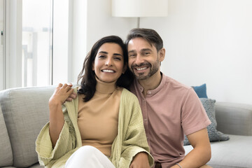 Portrait of multiethnic loving couple hugging seated on comfortable sofa