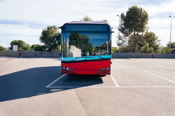 Modern red electric bus standing in a sunny empty parking lot, representing sustainable public...