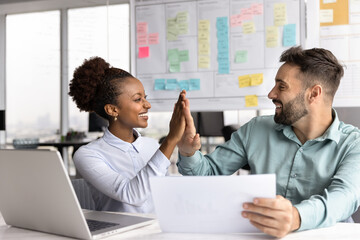 Diverse teammates celebrate milestone with high five at office desk