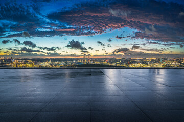 Empty square floor overlooking a large industrial area and city lights at twilight.