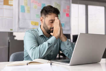 Burned out overworked male professional sitting by notebook feeling crisis
