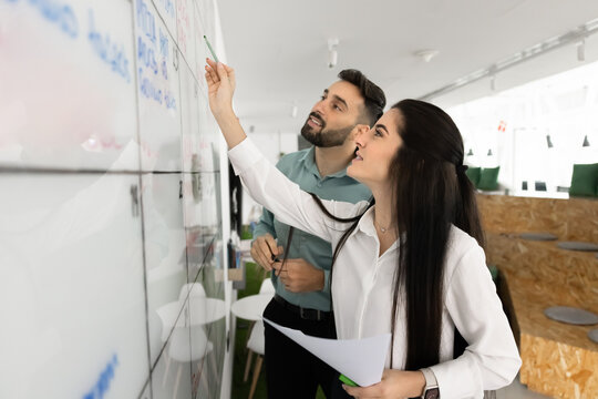 Smiling young business partners writing on whiteboard wall using markers