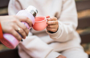 Cute child girl with thermos cup filled with hot tea on a cold autumn day.